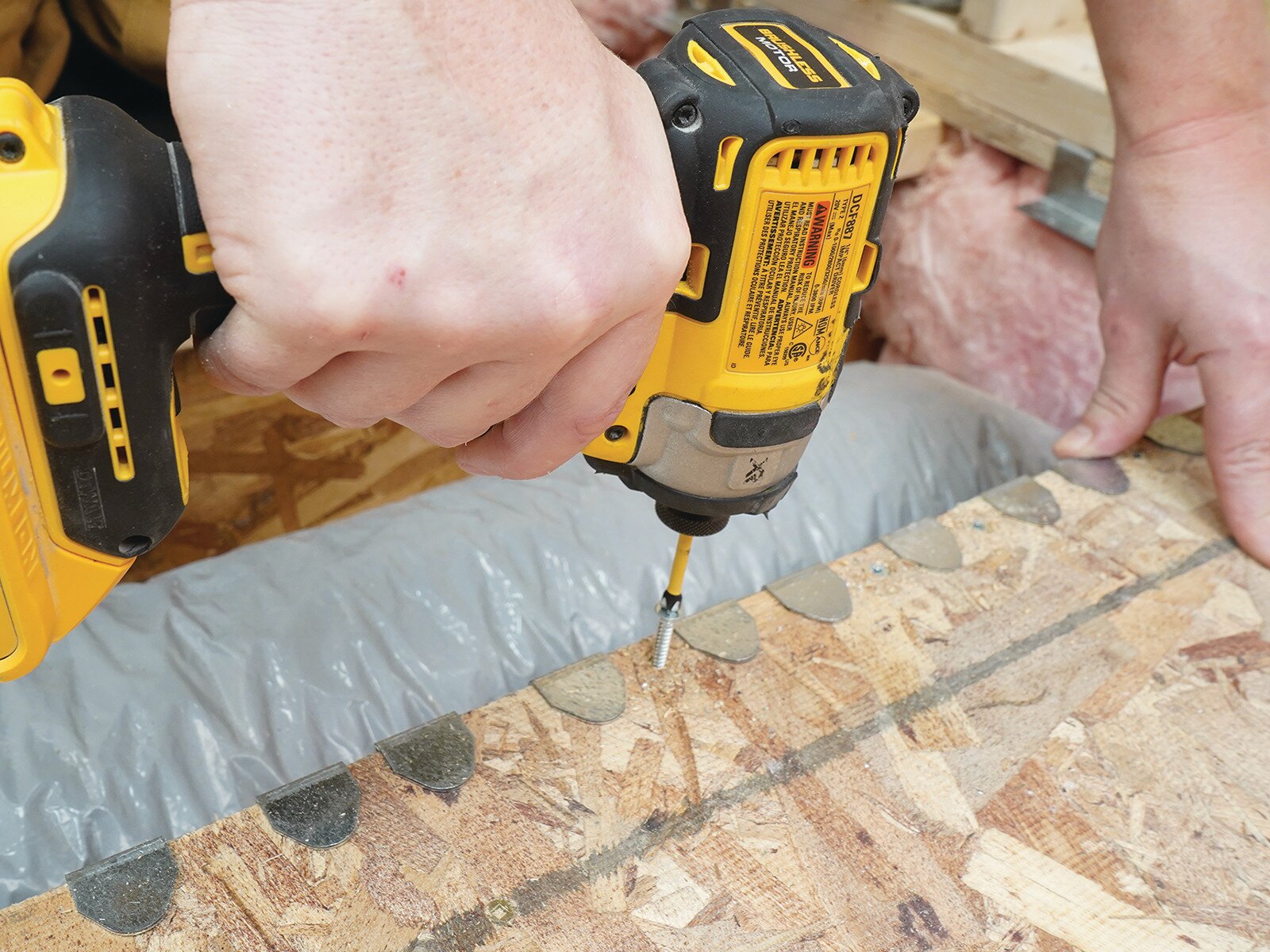 Installer fastening a Schluter Systems KERDI-SHOWER-FRS bracket above existing ductwork in the joist space