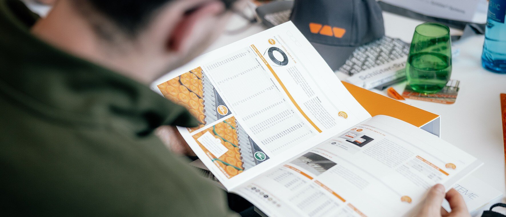 View over a man`s shoulder sitting on a desk, having a Schl&uuml;ter-Systems catalogue in his hands and looking at a DITRA-HEAT product page