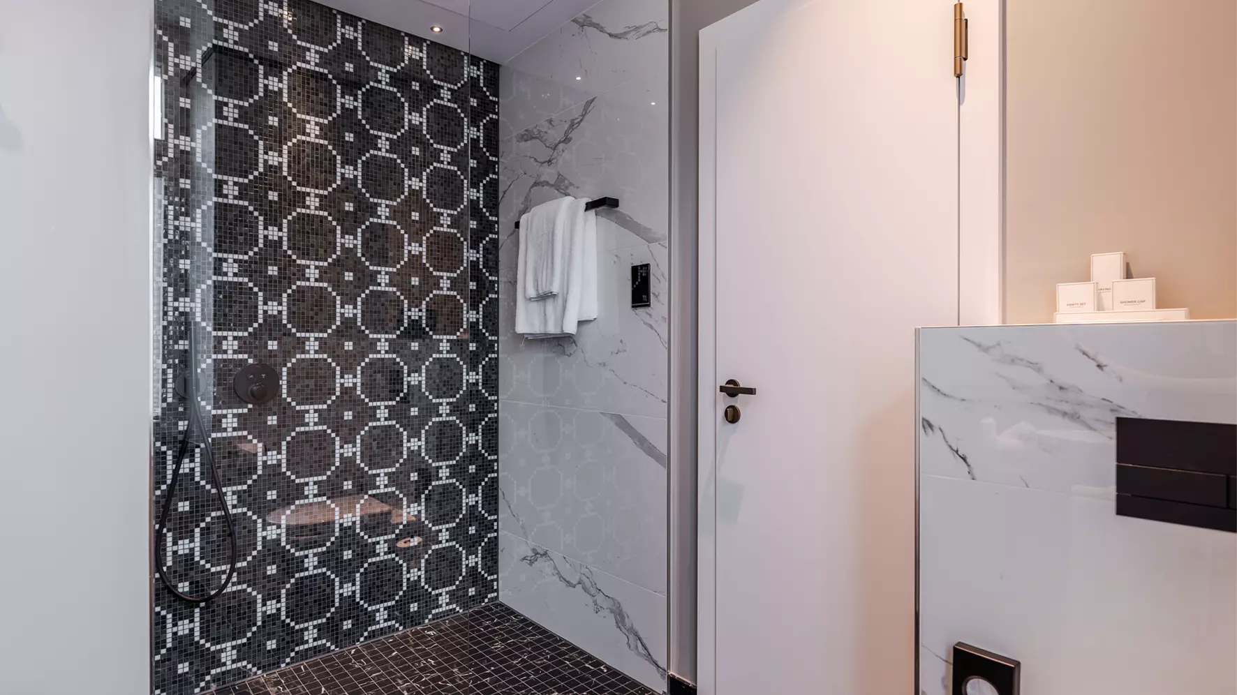 Cuarto de ba&ntilde;o terminado tras la renovaci&oacute;n con baldosas decorativas oscuras en la ducha y baldosas de m&aacute;rmol blanco en las paredes
