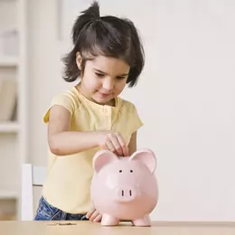 Klein meisje met donker haar gooit geld in haar spaarvarken.