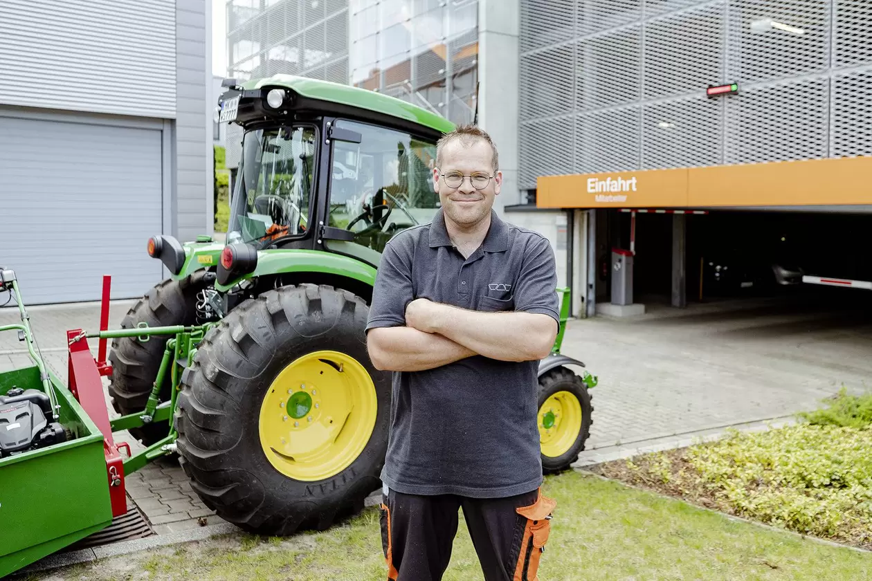Mitarbeiter steht vor einem kleinen gr&uuml;nen Traktor 