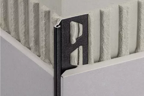 Vue d&eacute;taill&eacute;e du profil&eacute; Schl&uuml;ter-FINEC en finition TRENDLINE MGS, noir graphite mat, sur un angle sortant de mur avec carrelage de couleur grise