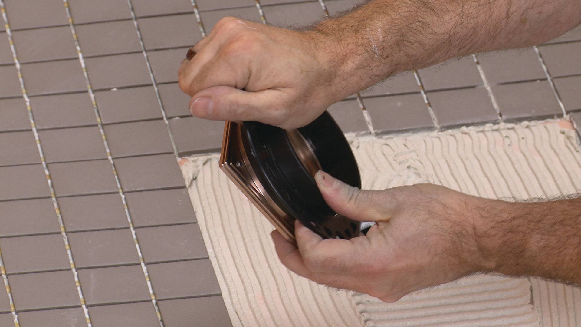 Un homme enclenche un collier de réglage de hauteur noir rond à l'arrière d'une grille de drain.