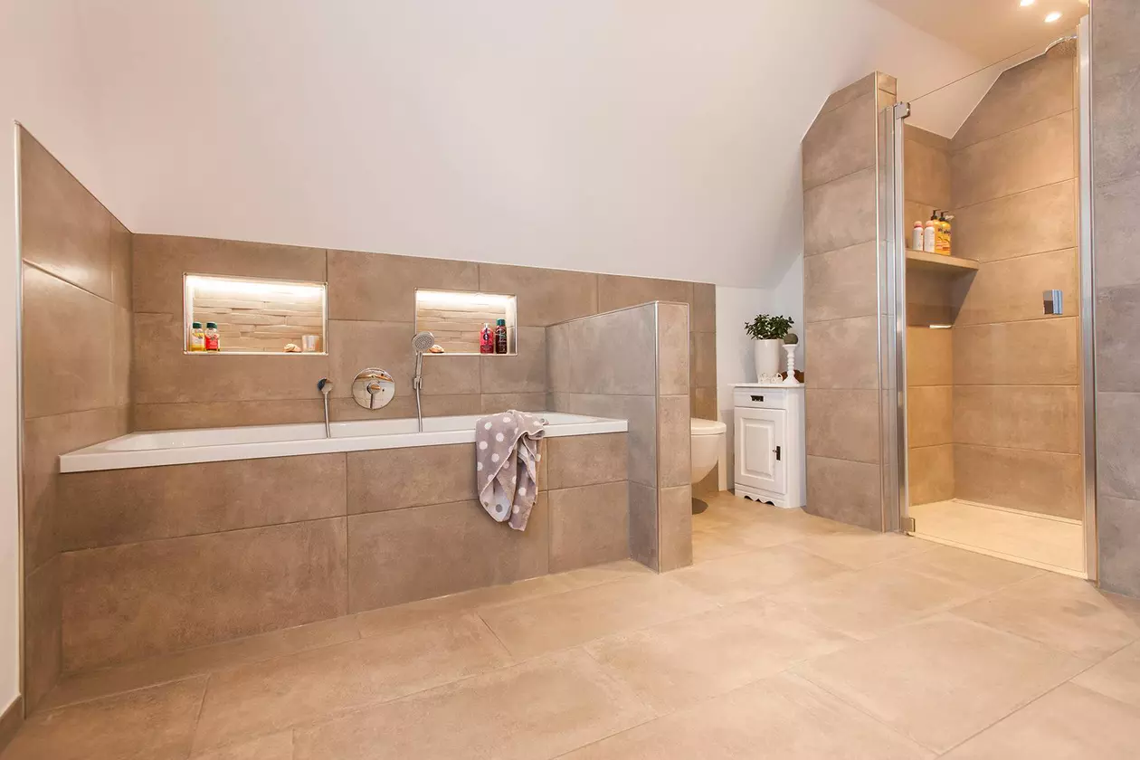 Pohled do koupelny s velkoform&aacute;tov&yacute;mi světl&yacute;mi dlaždicemi, vanou a oddělen&yacute;m sprchov&yacute;m koutem v &uacute;rovni podlahy