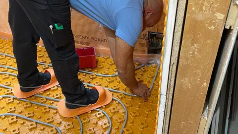Een vakman legt de kabels van de klimaatregelende tegelvloer BEKOTEC-THERM-EN F.