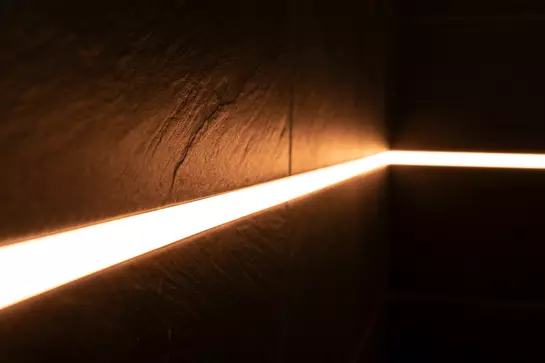 Nahaufnahme einer warm leuchtenden Lichtlinie an einer Wand mit dunklen Fliesen
