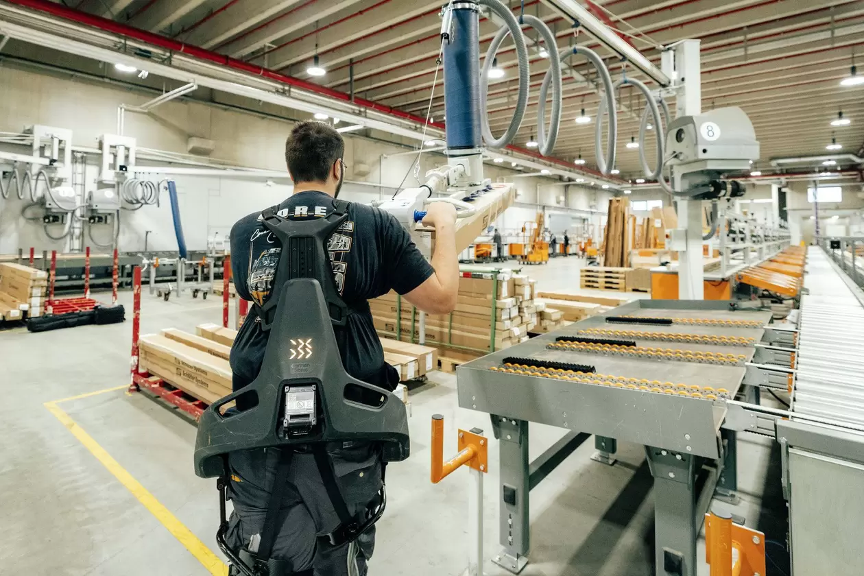 R&uuml;ckansicht eines Mitarbeiters in der Logistik, der ein Exoskelett benutzt