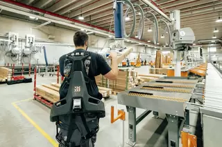 R&uuml;ckansicht eines Mitarbeiters in der Logistik, welcher ein Exoskelett nutzt