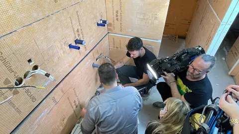 Een camerateam filmt twee vakmensen die de gelegde water- en waterafvoerleidingen beoordelen.