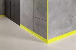 Close-up van een grijs betegelde buitenhoek van een wand met gele plint- en wandprofielen