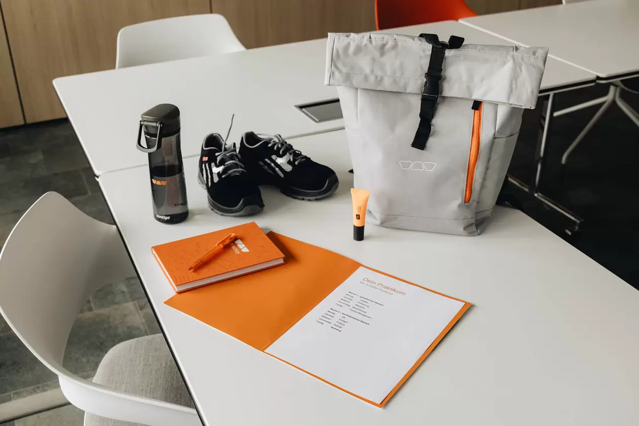 Materialien f&uuml;r Praktikanten stehen auf einem Tisch bereit: Rucksack, Trinkflasche, Schreibutensilien, Praktikumsplan und Sicherheitsschuhe