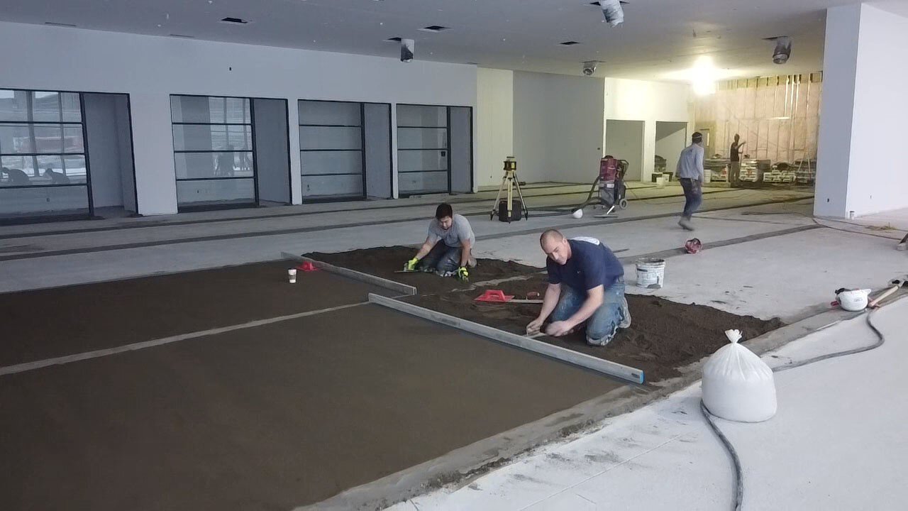 Deux personnes nivellent le sol de la salle d'exposition Lamborghini Montréal.