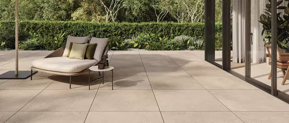 Terras met grote beige tegels, een stoel en een tafel voor een grote glazen deur.
