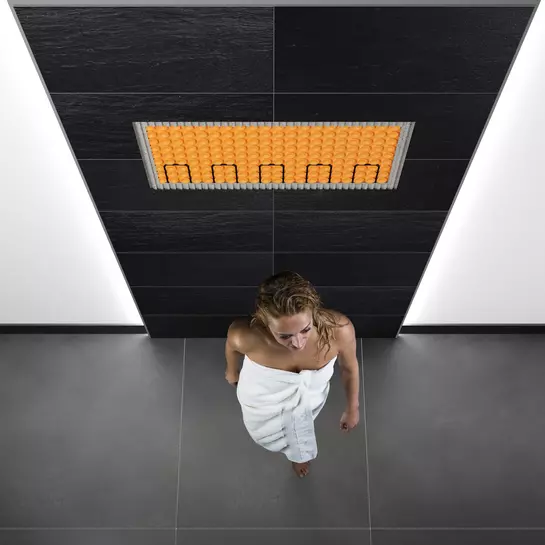 Vrouw in de badkamer voor een met DITRA-HEAT-E verwarmd wandoppervlak.