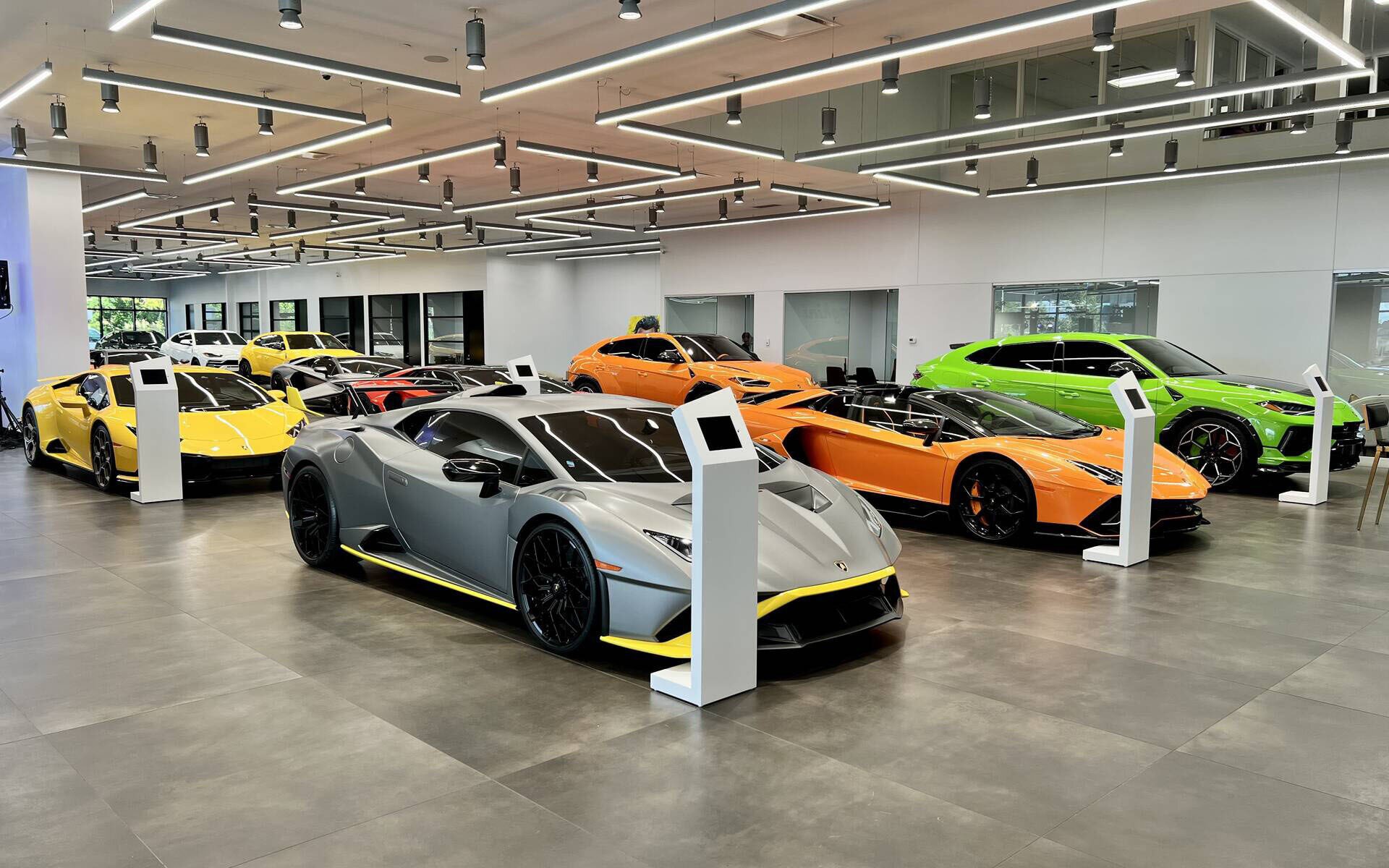 Une vue de la salle d'exposition Lamborghini Montréal présentant des Lamborghinis grises, oranges, vertes et jaunes.