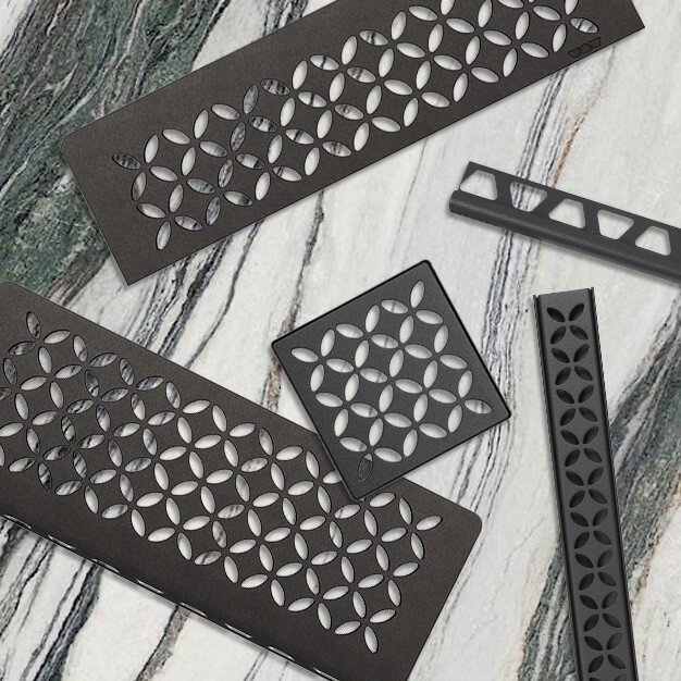 Étagères de douche anthracite foncé et caches de drain avec un motif floral disposés sur un carrelage en marbre.