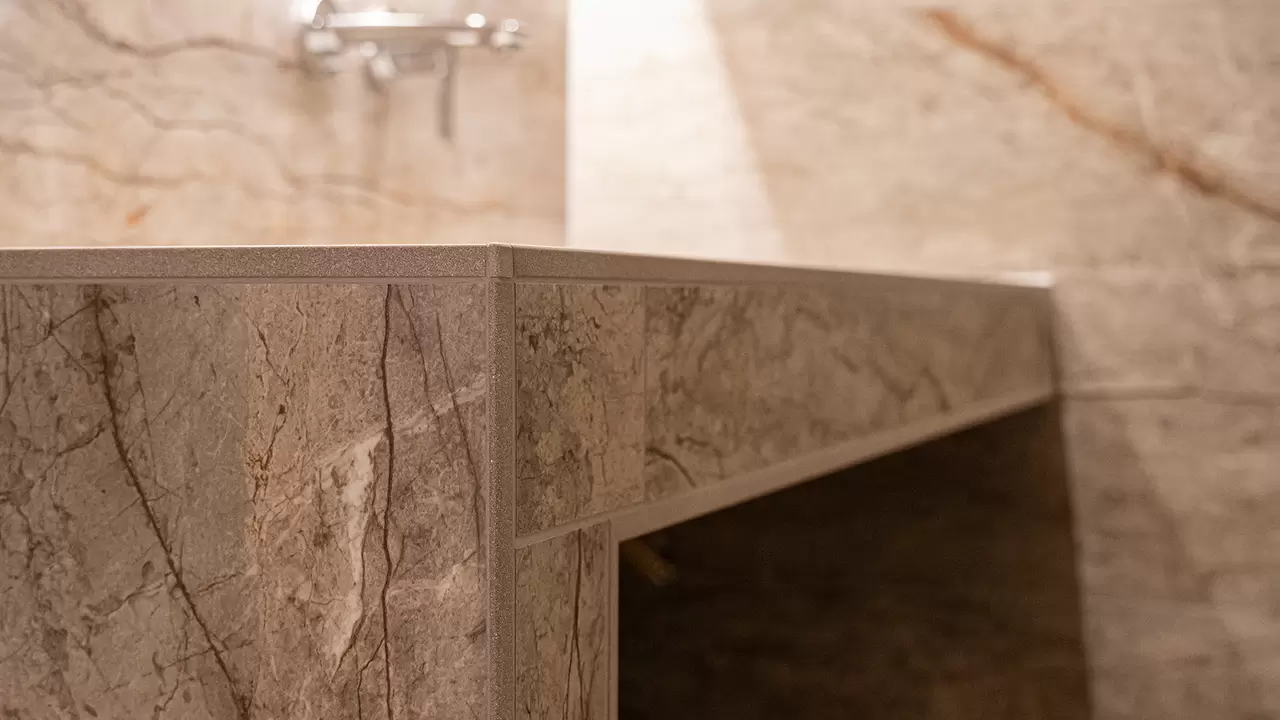 Gros plan sur le bord du lavabo dot&eacute; d'un carrelage d'aspect marbre beige et un profil&eacute; de finition Schl&uuml;ter-JOLLY assorti