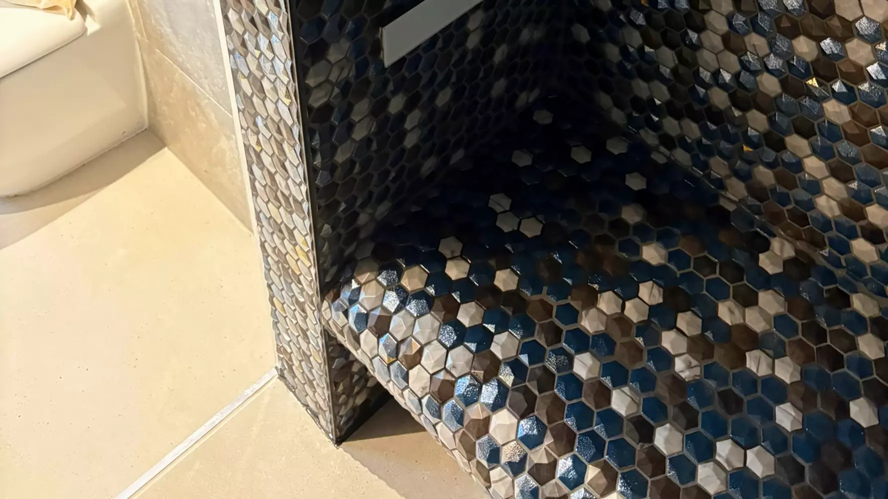 Bench in a shower tiled with blue, white and grey hexagon shaped tiles