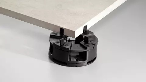 Een beige terrastegel steunt op een zwarte TROBA-LEVEL-PLA 30 hoogte-adapter