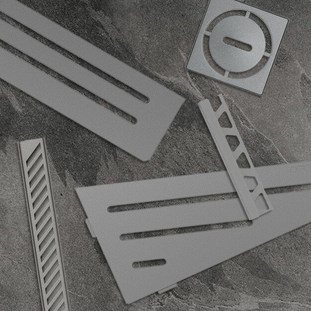 Une présentation de grilles de drain, étagères et profils couleur étain assortis sur un carrelage en marbre gris.