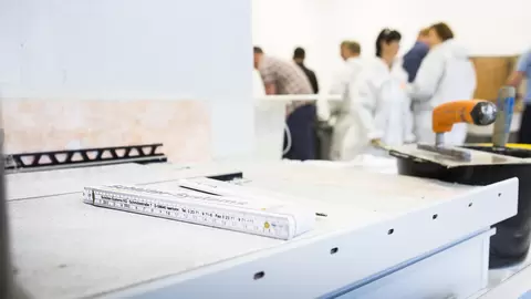 Ebene Arbeitsfl&auml;che in eimem Schulungsraum mit Profilkante, Zollstock, Kelle, Spachtel und Schulungsteilnehmern im Hintergrund