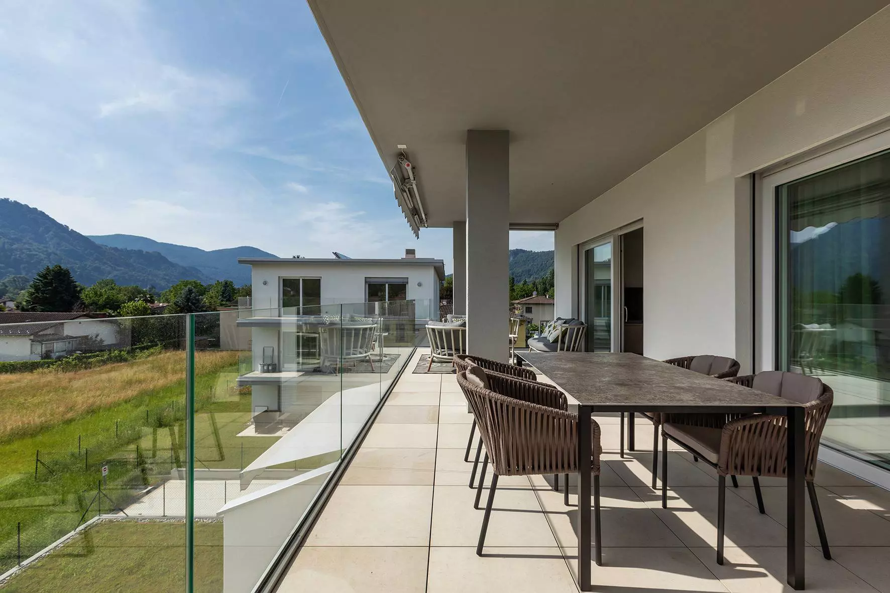 Licht betegeld balkon met een grote eettafel, op de achtergrond uitzicht op het groen en een bergpanorama