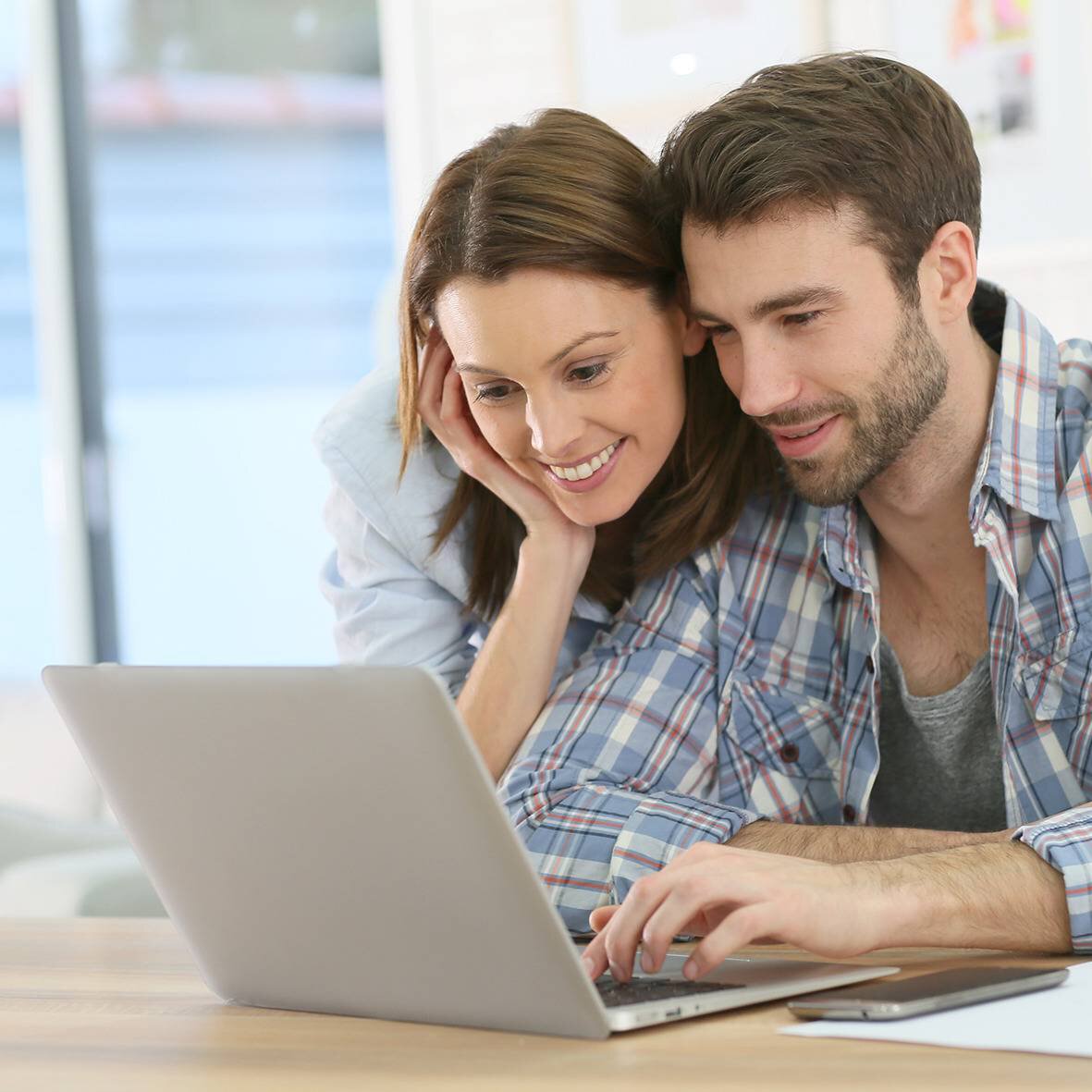 Un jeune couple est assis, de bonne humeur, devant un ordinateur portable ouvert
