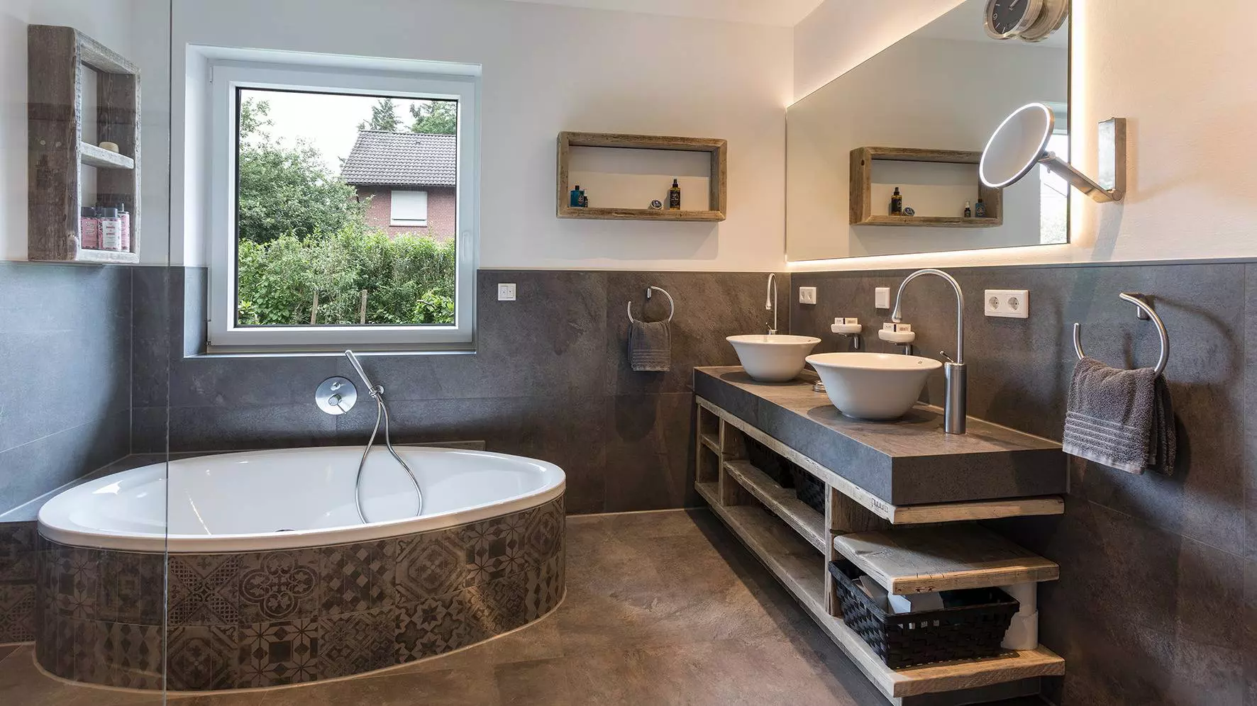 Foto van de gerenoveerde badkamer met bad, wastafelinstallatie en een verlichte spiegel.