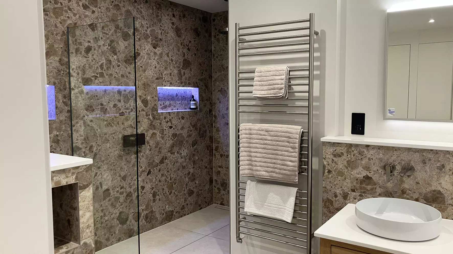 Finished renovated bathroom with large marble tiles, shower with illuminated niche and wash basin