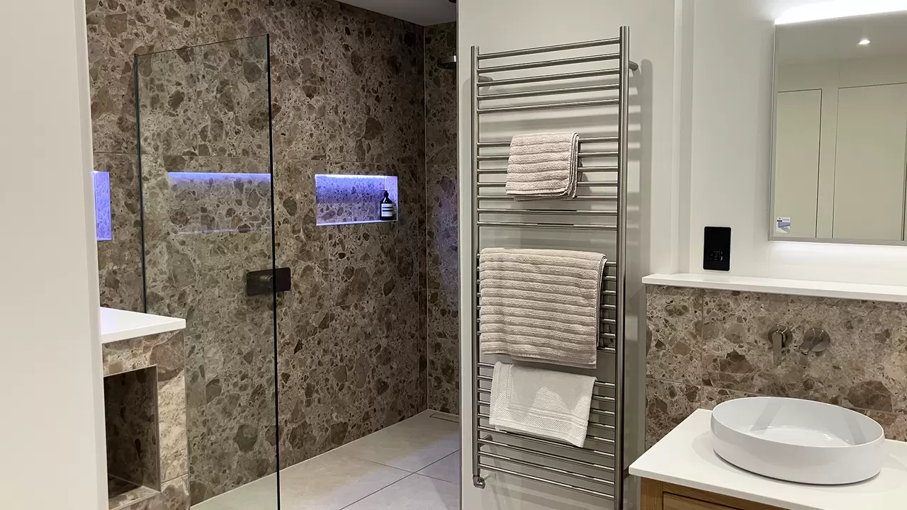 Finished renovated bathroom with large marble tiles, shower with illuminated niche and wash basin