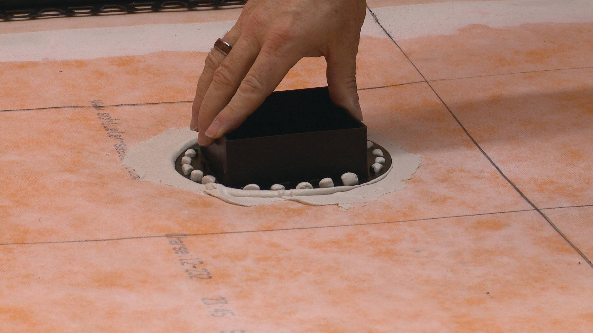 Une personne se prépare à poser des carreaux, en utilisant un espaceur au-dessus d'un drain.