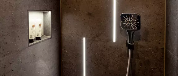 Dunkelgrau geflieste Dusche mit beleuchteter Wandnische und beleuchteten Lichtprofilen an der Wand hinter der Armatur