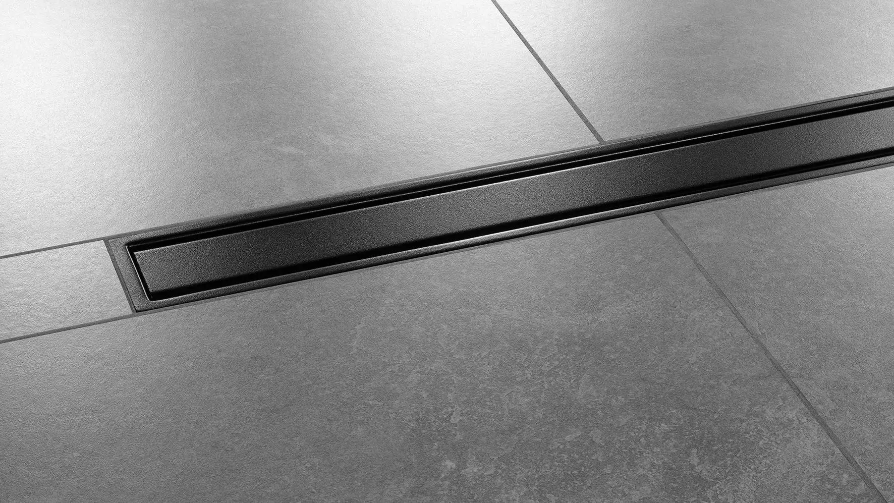 Gros plan sur un sol de douche avec carrelage de couleur gris fonc&eacute; et caniveau Schl&uuml;ter-KERDI-LINE-A install&eacute; au centre de la douche, design SOLID, finition TRENDLINE, noir graphite mat.