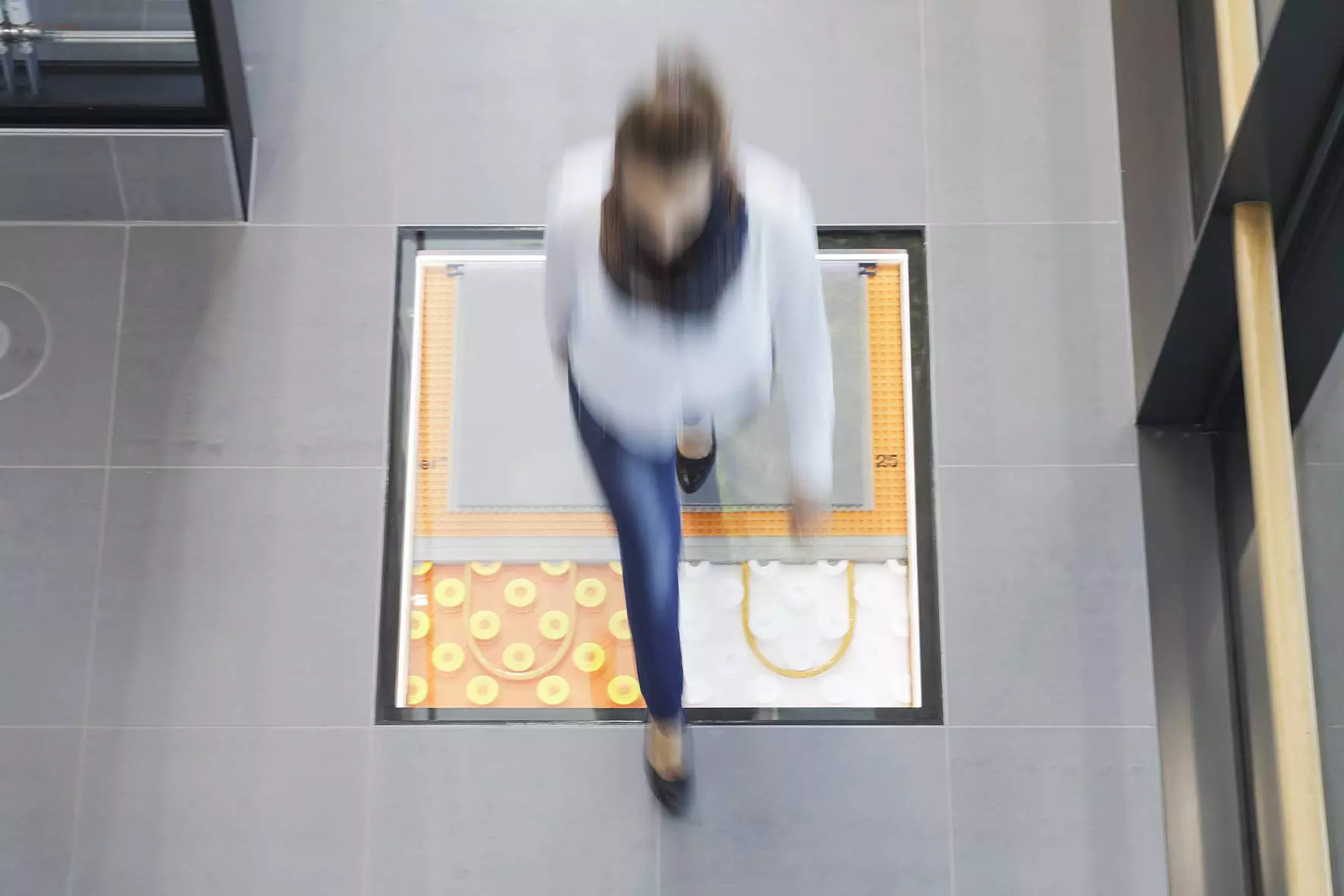 Een vrouw loopt over een vloer, waarin door glaselementen verschillende verwarmingssystemen in de onderbouw zichtbaar worden