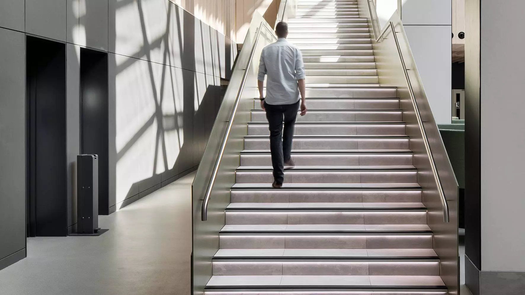 Een man loopt een trap op waarvan de treden indirect worden verlicht door Schl&uuml;ter-LIPROTEC
