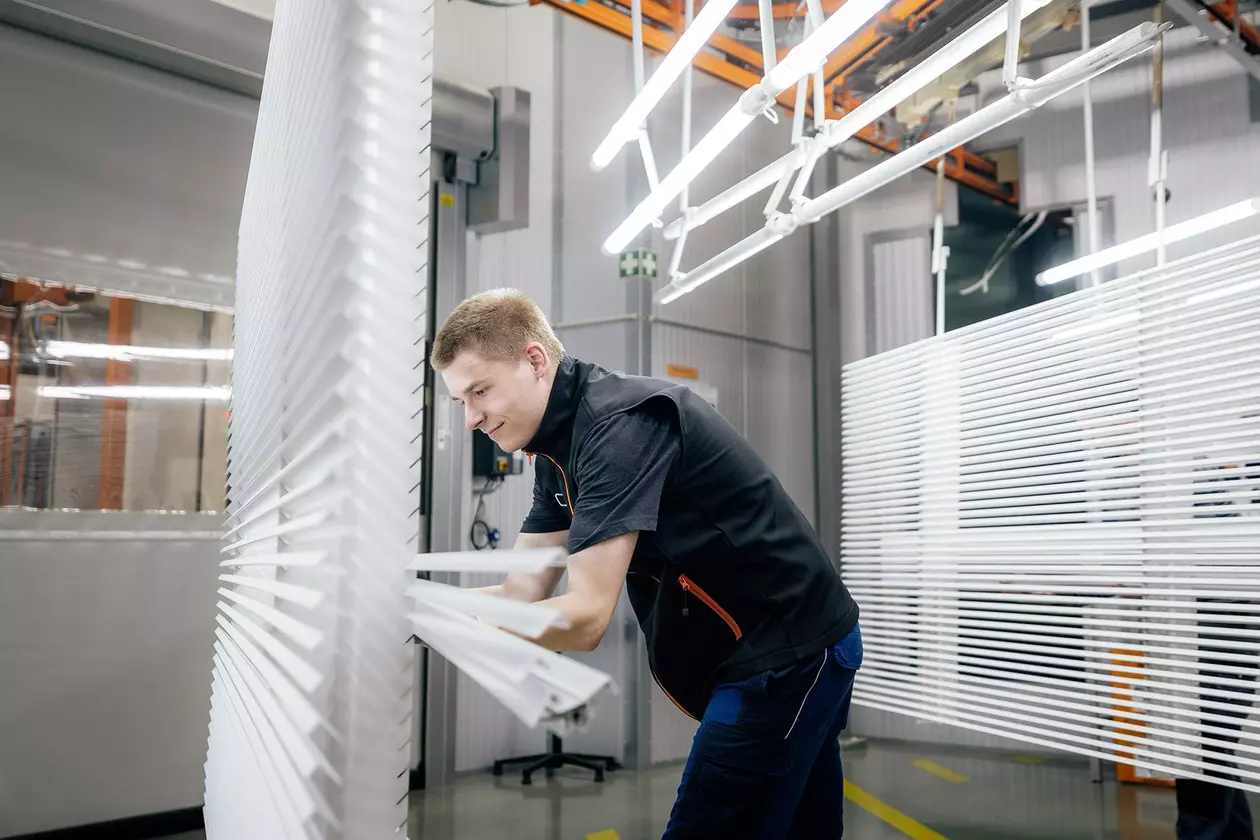 Ein Mann in Arbeitskleidung pr&uuml;ft in hellem Licht die Beschichtung von Abschlussprofilen