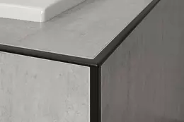 Esquina de un borde de ba&ntilde;era alicatado con perfil de remate negro y baldosas gris claro