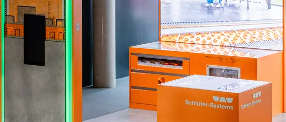 Zu sehen ist ein Teil des Ausstellungsmoduls BEKOTEC-CompetenceCenter, unter anderem mit verbauten Produktmustern, Videowand und Schl&uuml;ter-Logo.