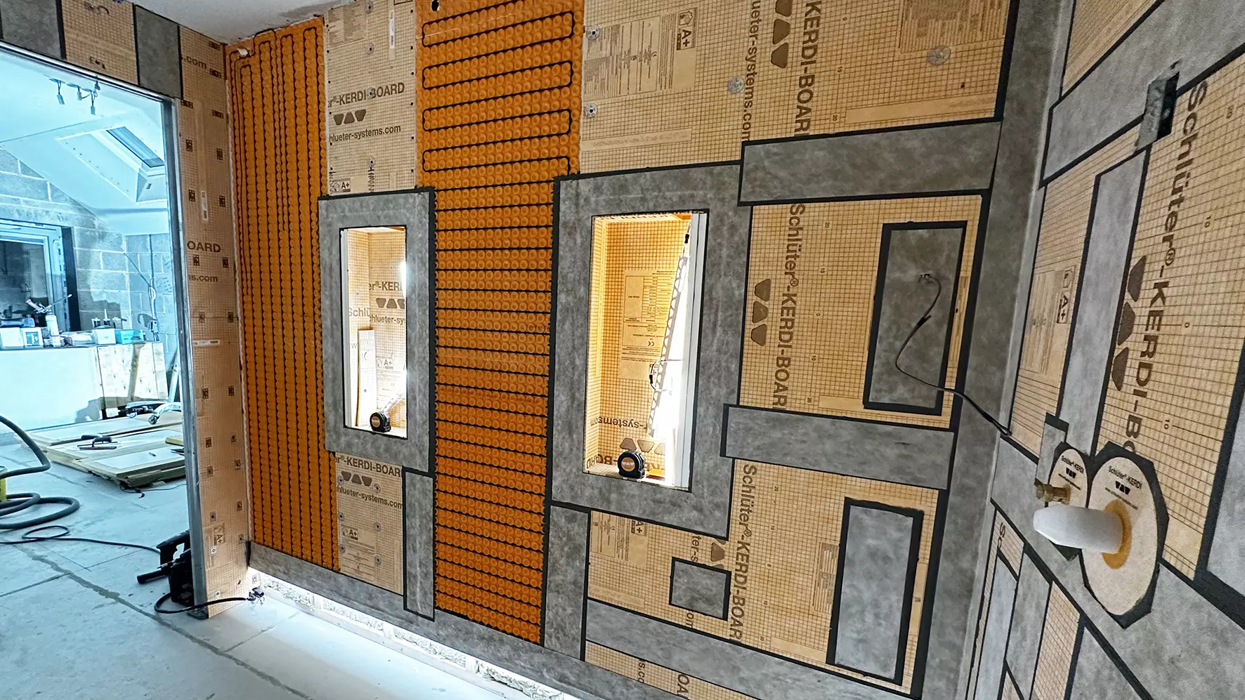 Bathroom construction site with LED-lit wall niches, orange uncoupling mat and heating cables on the wall