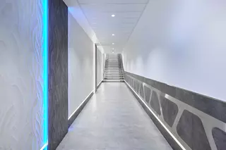 Hell beleuchteter Flur mit blauen Lichtakzenten und einer Treppe mit beleuchteten Stufen am Ende des Ganges