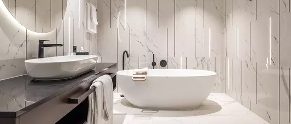 Badezimmer im Hotel Steigenberger Hof mit wei&szlig;en Marmorfliesen, freistehender Wanne und Schl&uuml;ter-LIPROTEC Lichtprofilen in der Wand