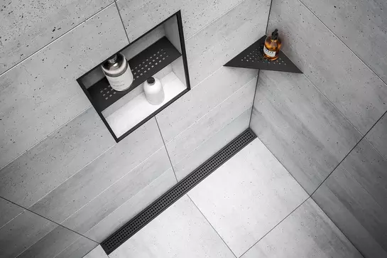 Illustration d'une douche carrel&eacute;e en aspect b&eacute;ton avec caniveau noir mat Schl&uuml;ter-KERDI-LINE, tablette de douche de la gamme Schl&uuml;ter-SHELF et niche avec profil&eacute; de finition noir mat.