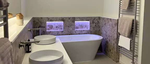 White bathtub with two illuminated niches in the wall above