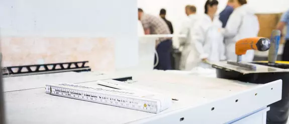 Ebene Arbeitsfl&auml;che in eimem Schulungsraum mit Profilkante, Zollstock, Kelle, Spachtel und Schulungsteilnehmern im Hintergrund