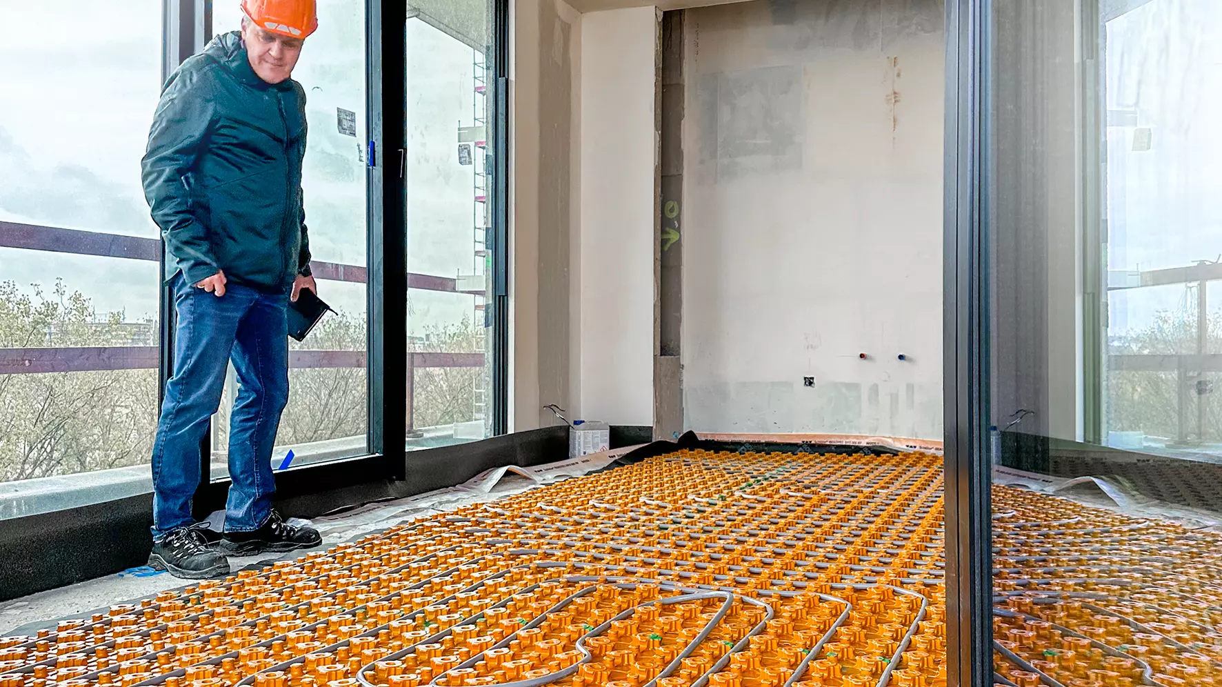 Ein Mann Schutzhelm blickt pr&uuml;fend auf die verlegte BEKOTEC-THERM Matte mit Heizrohren in einem Raum der City Dox