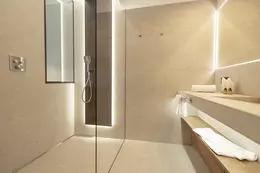 Salle de bain carrel&eacute;e de beige avec douche &agrave; l’italienne et lavabo avec grand miroir