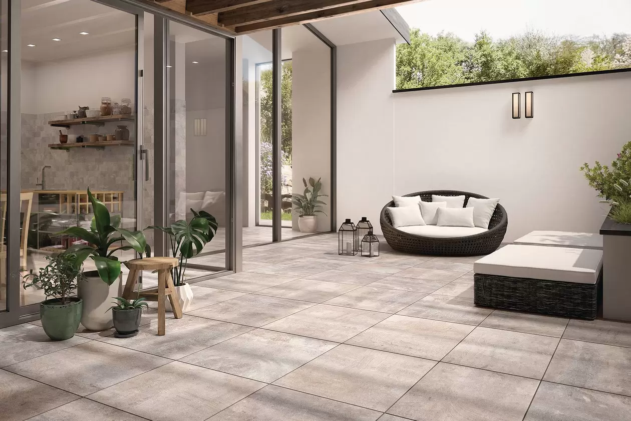 Außenansicht einer hochmodernen Terrasse als Erweiterung des Wohnbereichs mit hellgrauen Fliesen, bequemen Loungemöbeln und Pflanzen sowie Dekorationsartikeln.