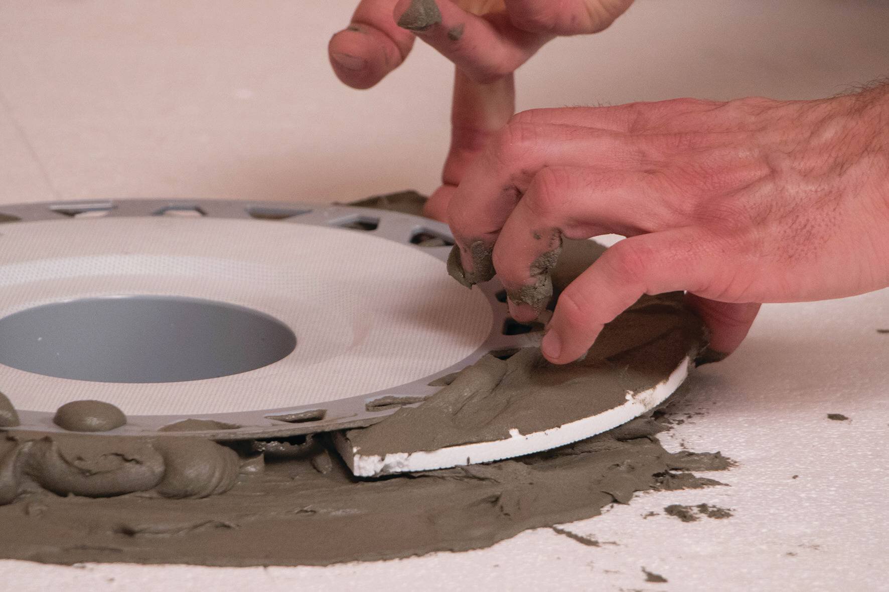 Les entretoises en mousse sont retirées d'une bride de drain encastrée dans le mortier Schluter Thin-Set.