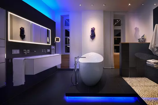Schwarz gefliestes Bad mit freistehender Badewanne und blauen Licktakzenten am Wannensockel und an der Decke