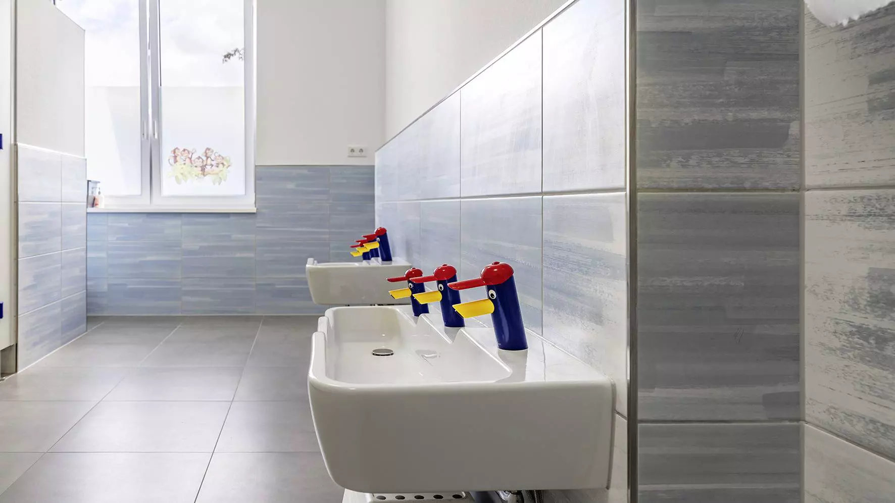 Kindgerechte Waschtische mit bunten Wasserh&auml;hnen in Entenform im Kindergarten der Marktschule
